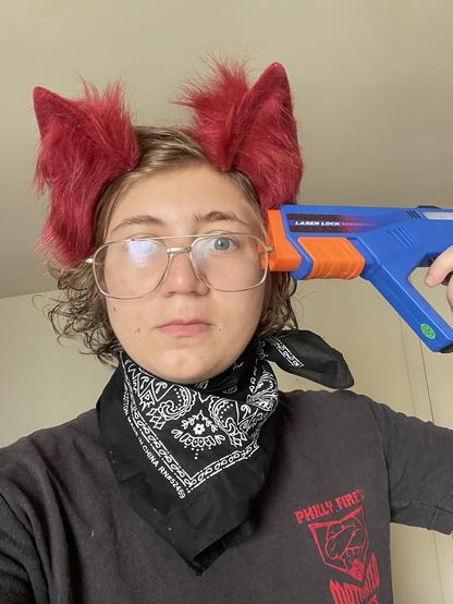 Guy with red wolf ears and a bandana holding a fake blue blaster gun to his head 
