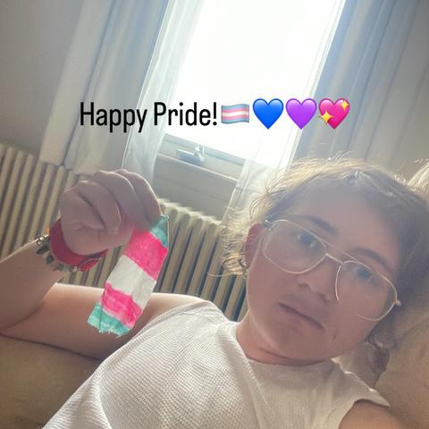 Man holding trans pride flag, caption says “Happy Pride” with trans flag and bi colored heart emojis